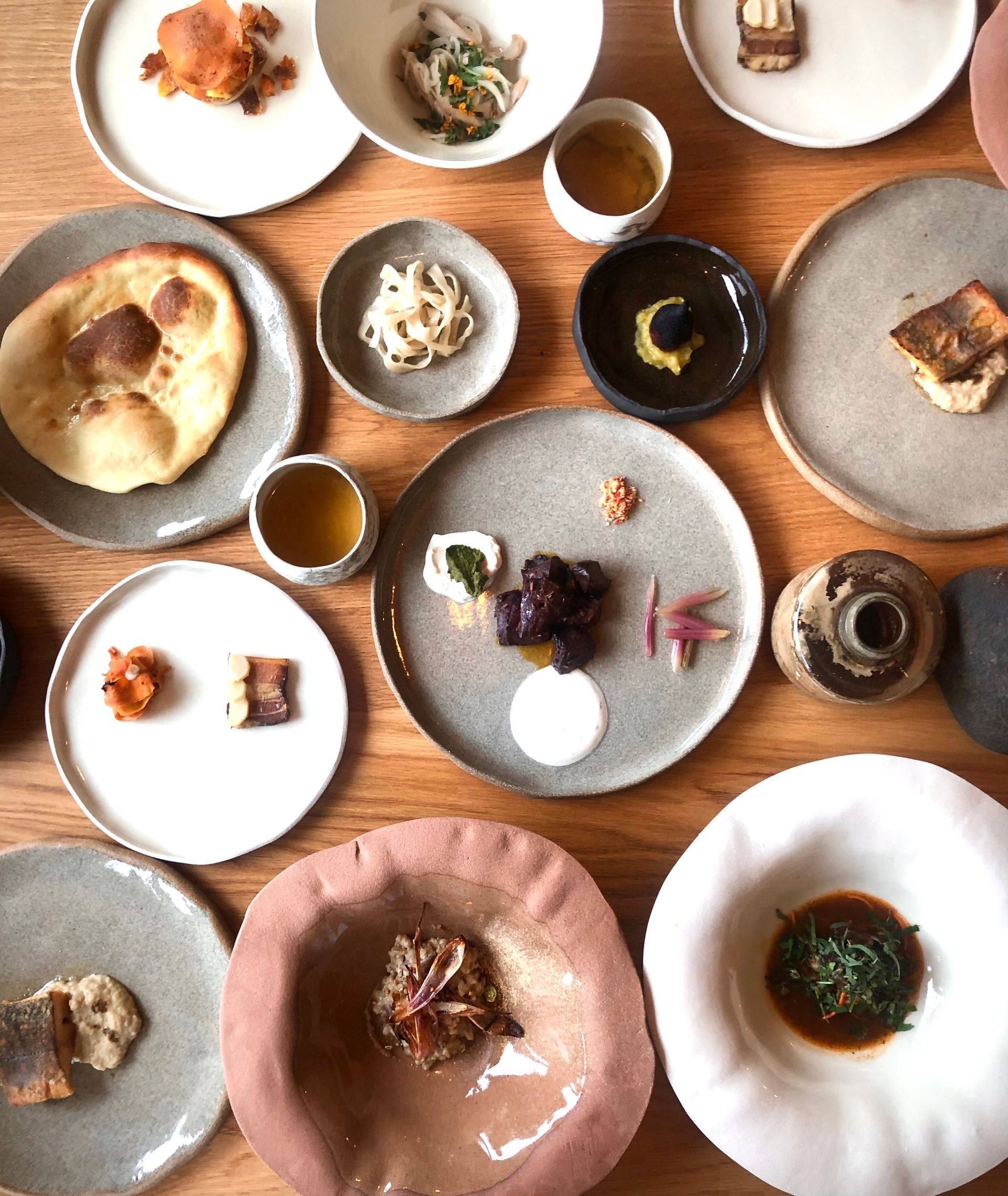 Vue aérienne d'une table en bois garnie de nombreuses petites assiettes de nourriture aux couleurs et textures variées.