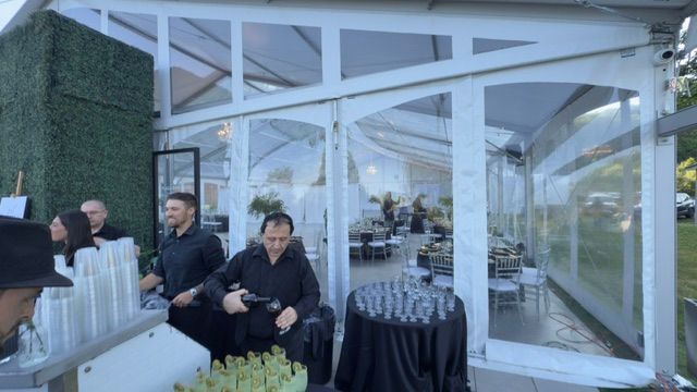 Des personnes préparent des boissons dans un bar éphémère installé sous une tente blanche, lors d'un événement en plein air.