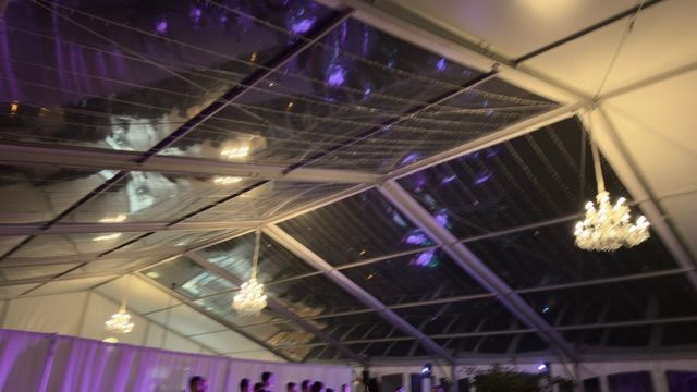 Sous une tente transparente, des lustres pendent du plafond. On aperçoit en dessous des rideaux blancs et des lumières violettes.