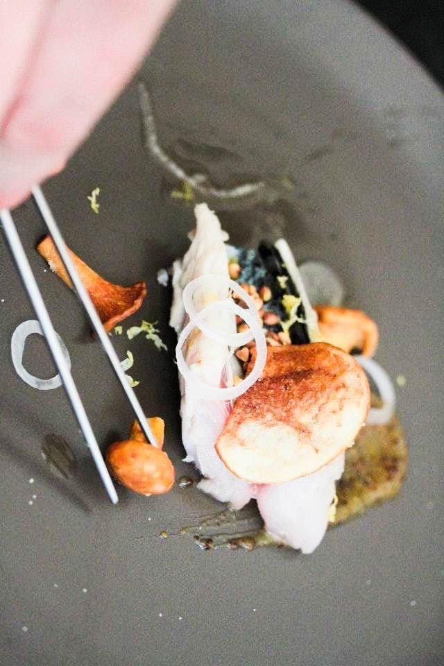 Gros plan sur un plat gastronomique composé de champignons, d'oignons et de sauce. Une paire de baguettes est disposée à proximité.