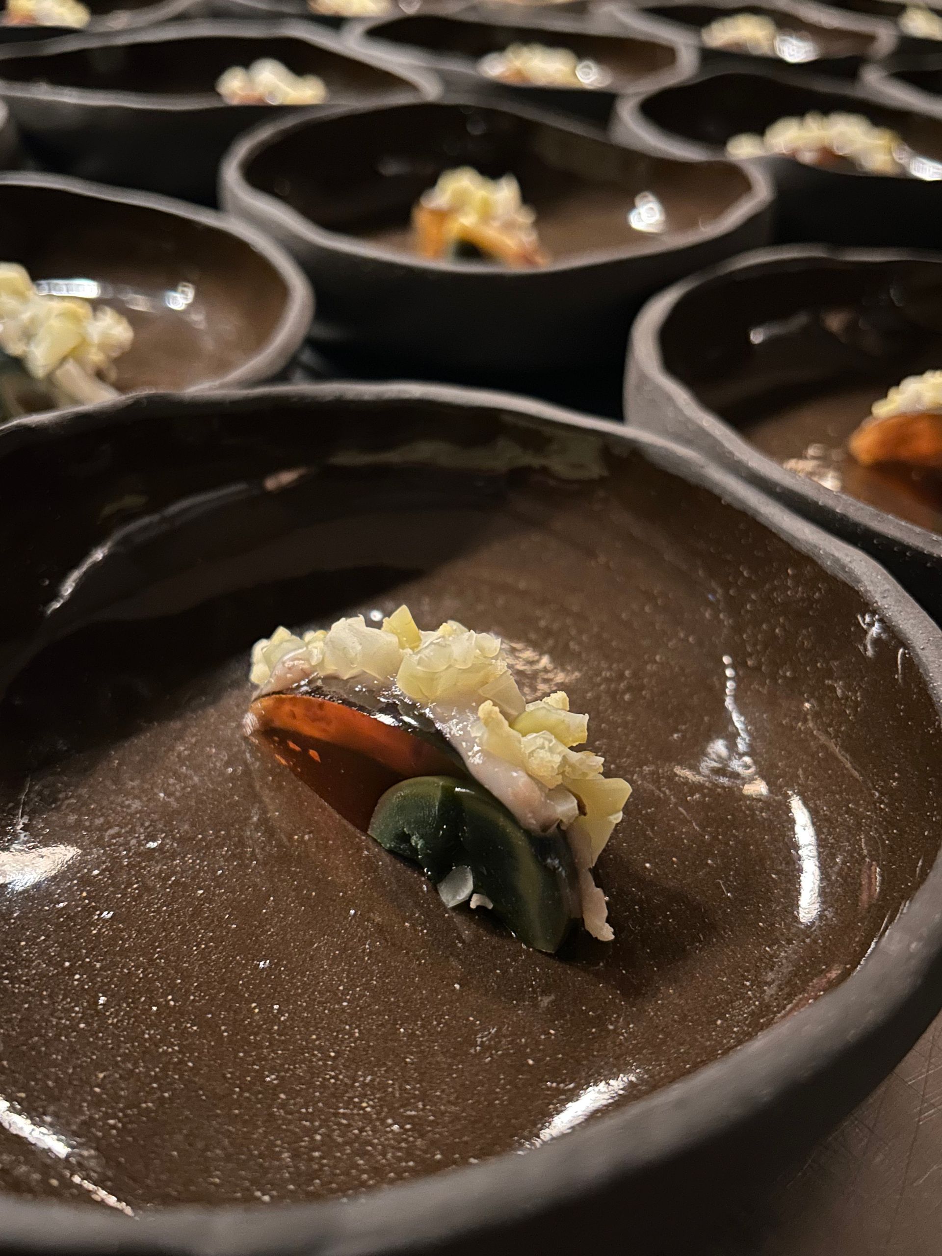 Gros plan sur de nombreux bols bruns, chacun contenant une petite portion de nourriture, dont une tranche recouverte de miettes jaunes.