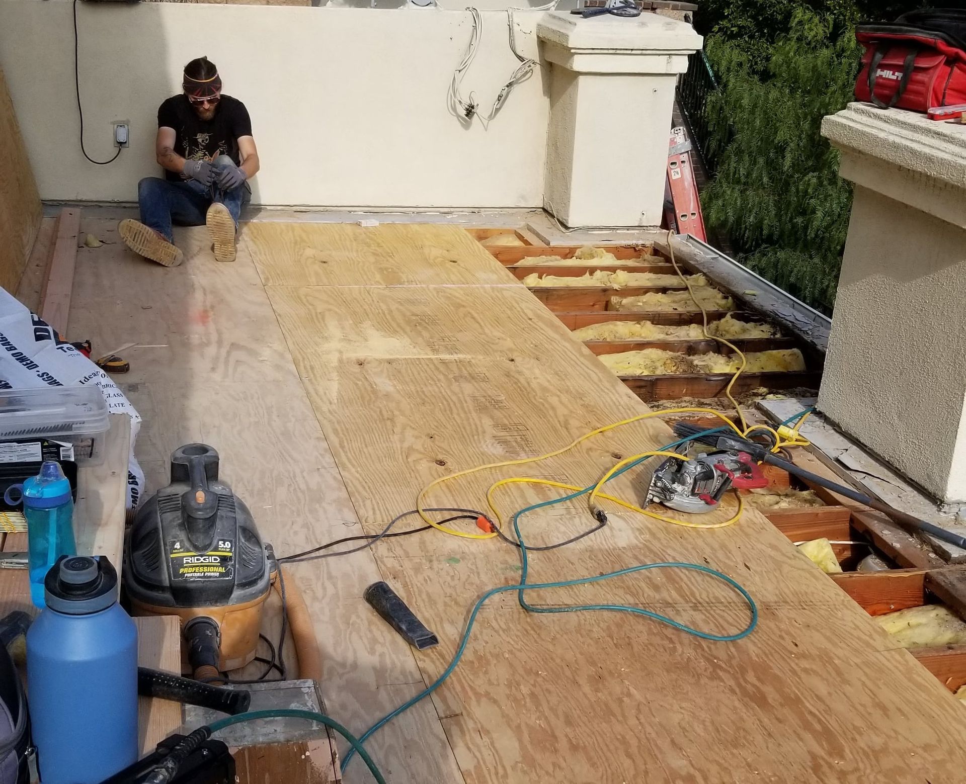 A man is sitting on a roof with a vacuum cleaner.