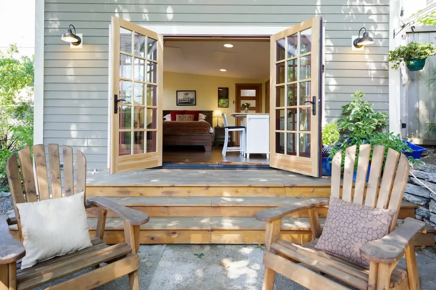 Two wooden chairs are sitting on a patio in front of a house with french doors open.