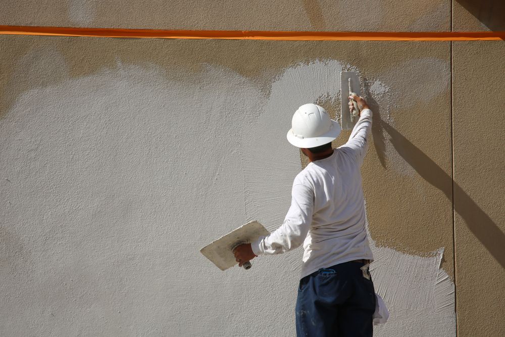 A man wearing a hard hat is plastering a wall with a trowel.