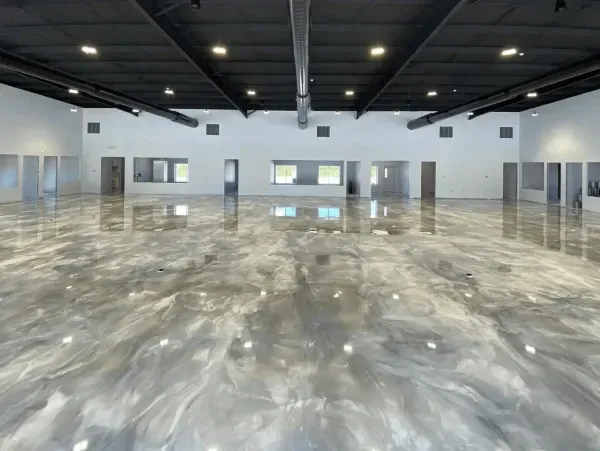 Wide, empty room with shiny, silver and white epoxy floor and dark ceiling.