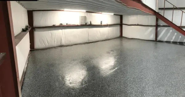Empty garage with a shiny, speckled floor, white walls, and metal beams.