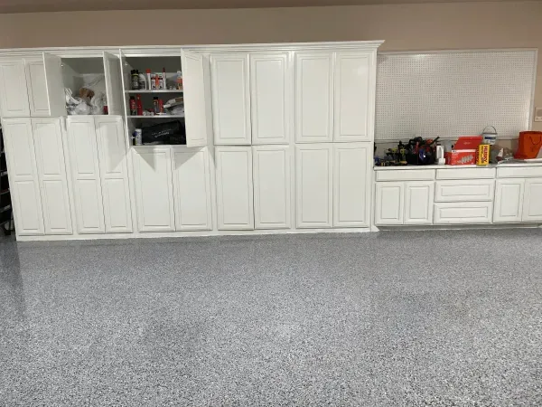 Garage with white cabinets on a speckled gray floor, with some cabinet doors open.