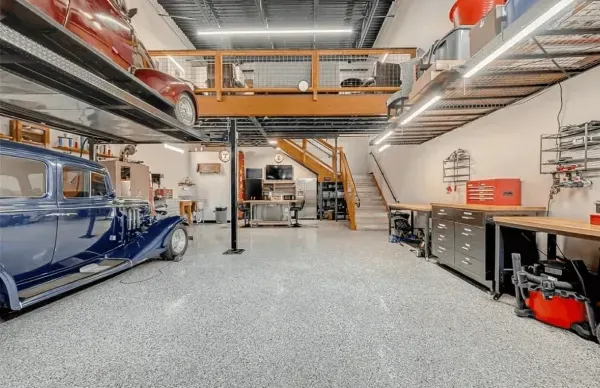 Garage with car lifts, workbench, and loft area. Blue and red classic cars. Gray epoxy floor.