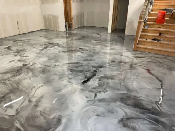 Shiny, marbled metallic epoxy floor in gray and white, in an unfinished room with stairs.