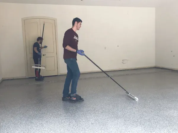 Two men applying epoxy flooring in a garage. One rolls the coating, the other moves behind him.