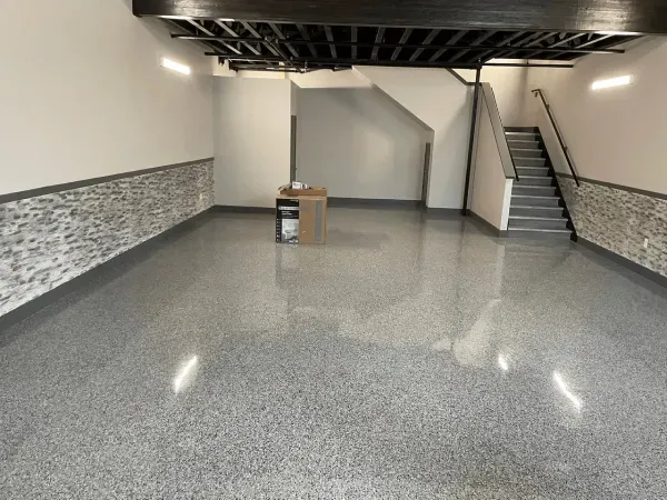 Spacious room with polished gray floor, stairs, and partial stone wall; a small table stands in the center.