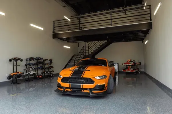 Orange Mustang in a garage with a mezzanine and racing karts.