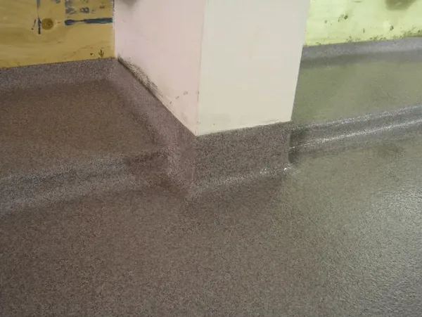 Gray speckled flooring meets a white wall, featuring a raised edge for sealing.