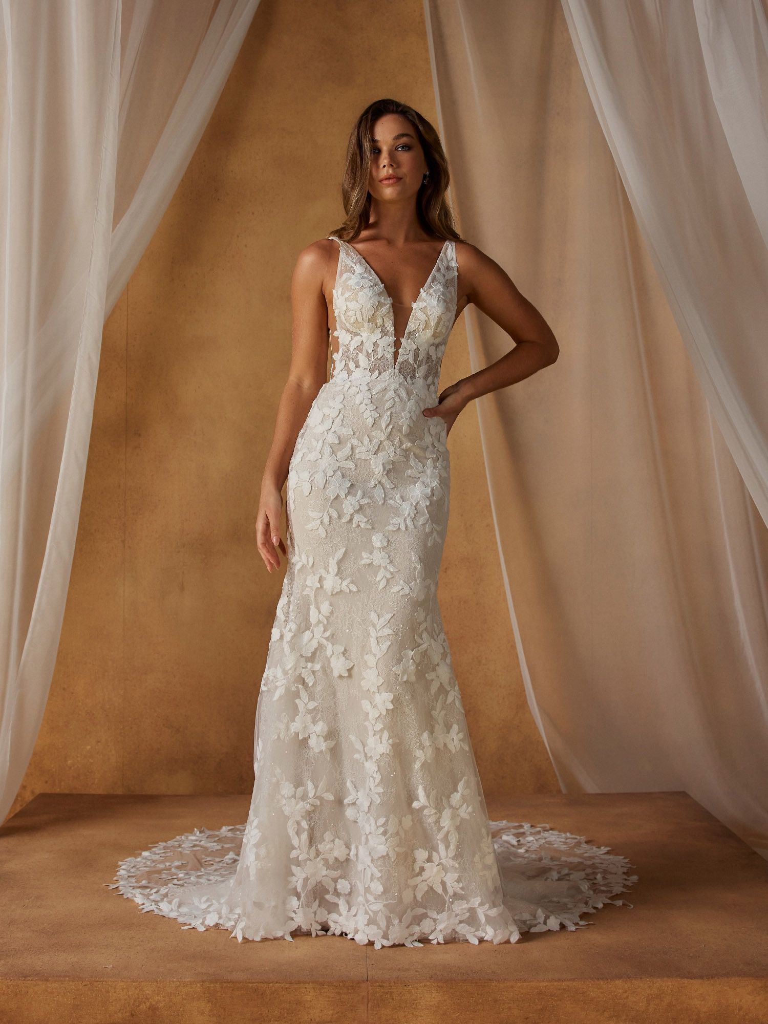 Nellie  van Madi Lane heeft een trompet silhouet met een laag glitter tule om een ​​extra glans toe te voegen aan haar all-over pailletten kantpatroon. Haar lijfje is ontworpen met een moderne, trendy piek-stijl halslijn met een sexy maar ingetogen illusie plunge. 