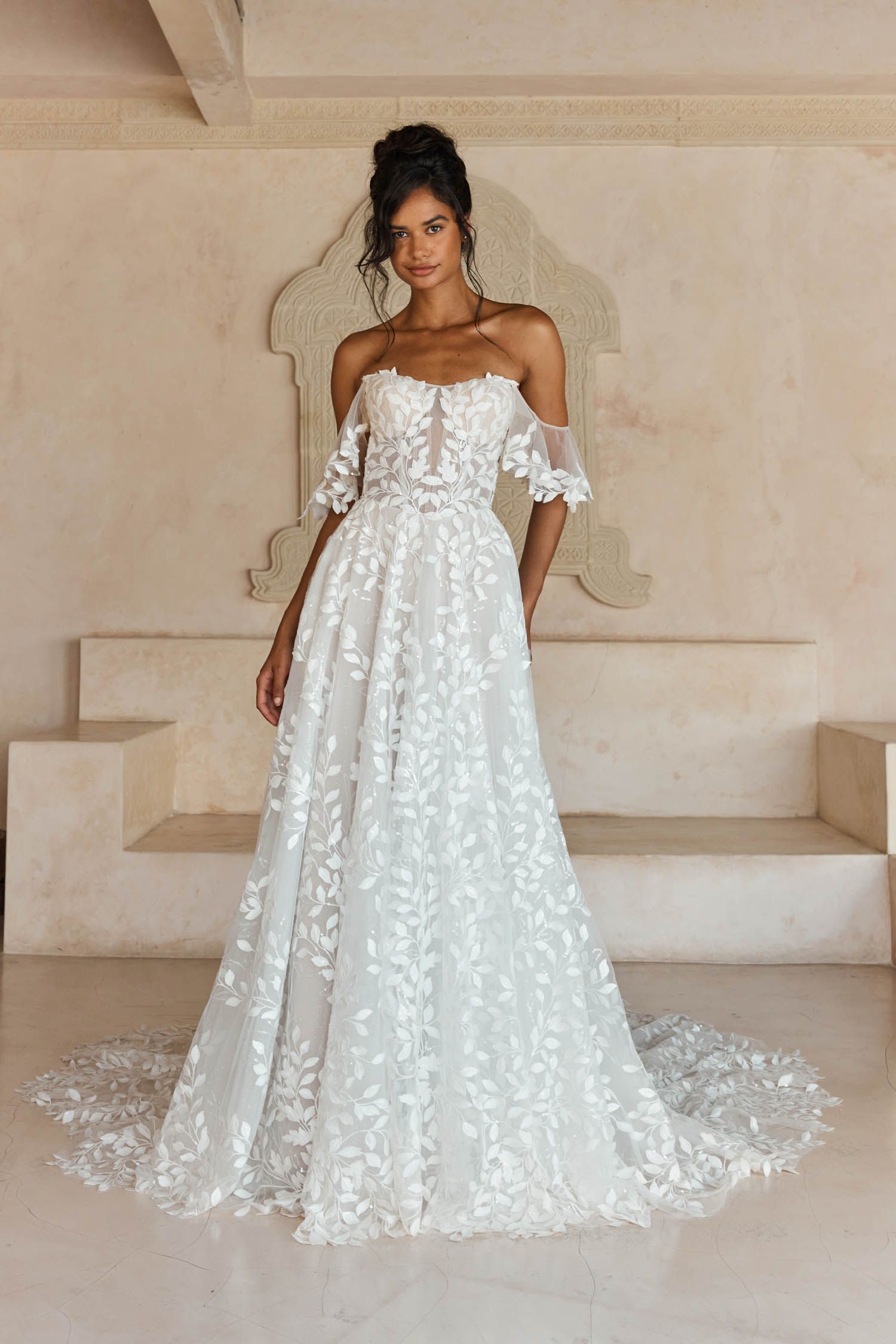 Laiya van Madi Lane heeft een A-lijn silhouet met een laag glitter tule om een ​​extra glans toe te voegen aan haar all-over pailletten kantpatroon. Haar lijfje is ontworpen met een moderne, trendy piek-stijl halslijn met een sexy maar ingetogen illusie plunge. 