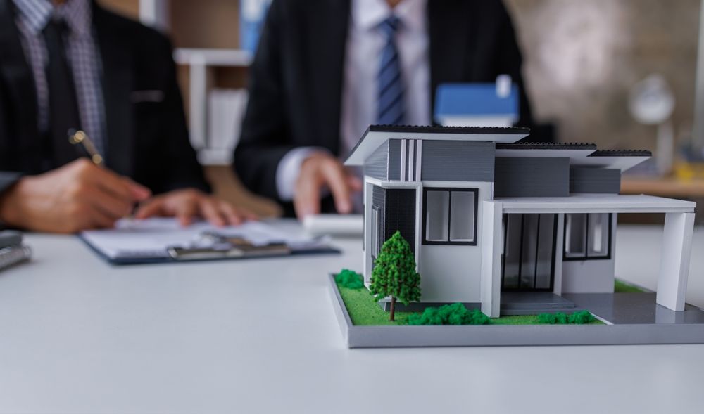 a man is sitting at a table with a model house and a clipboard