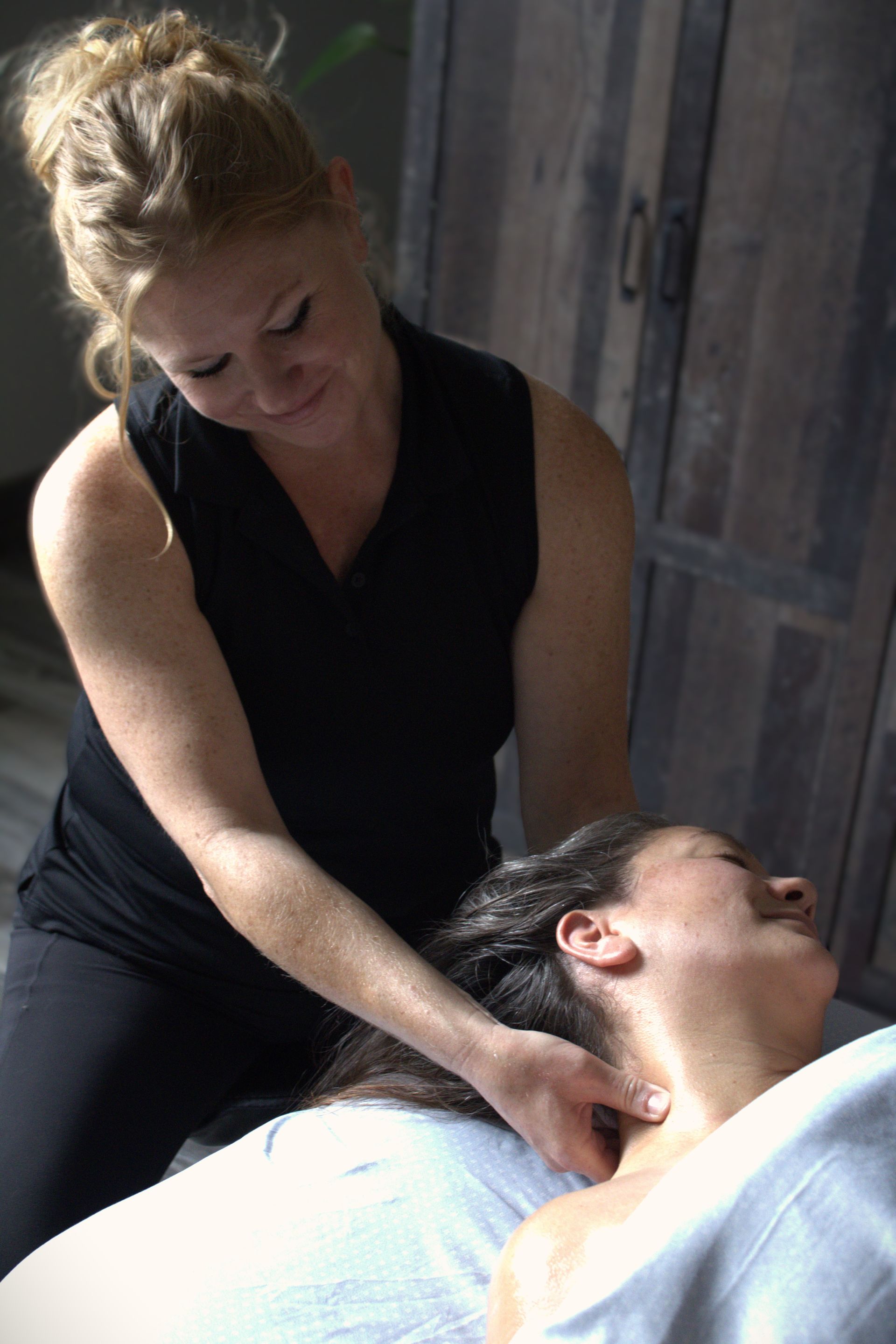 Woman giving neck massage to person lying down on a massage table.
