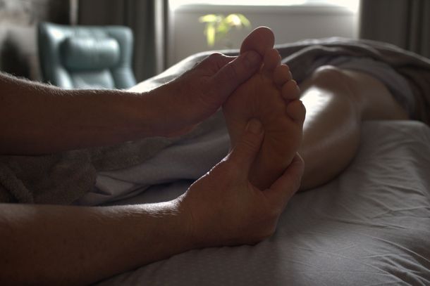 Hands massaging a foot on a massage table. The person is indoors.