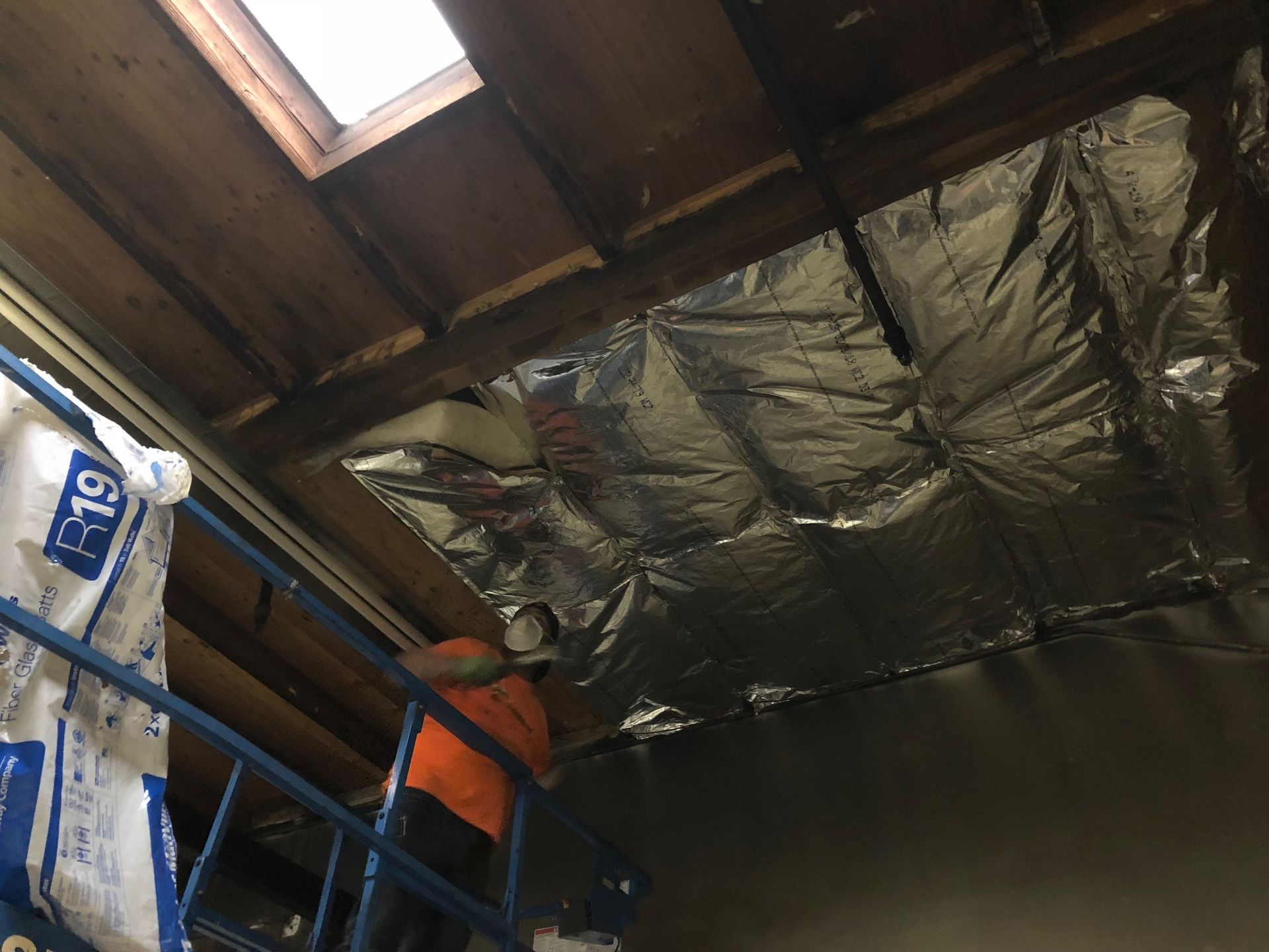A man is standing on a ladder looking up at a ceiling covered in aluminum foil.