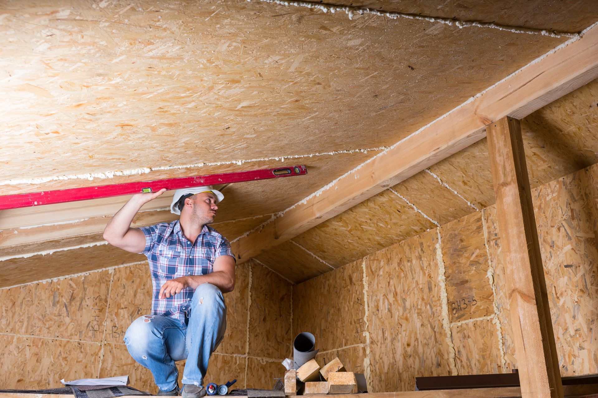 A man is measuring the ceiling of an attic with a level.