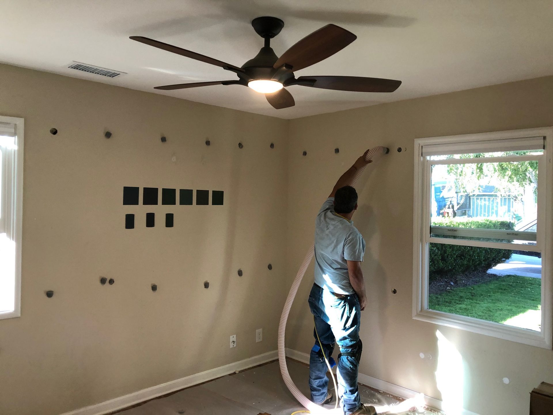 A man is blowing insulation into a room with a ceiling fan.