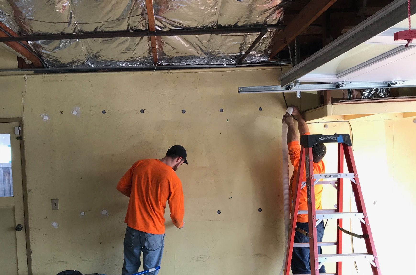 Two men are working on a wall with a ladder.