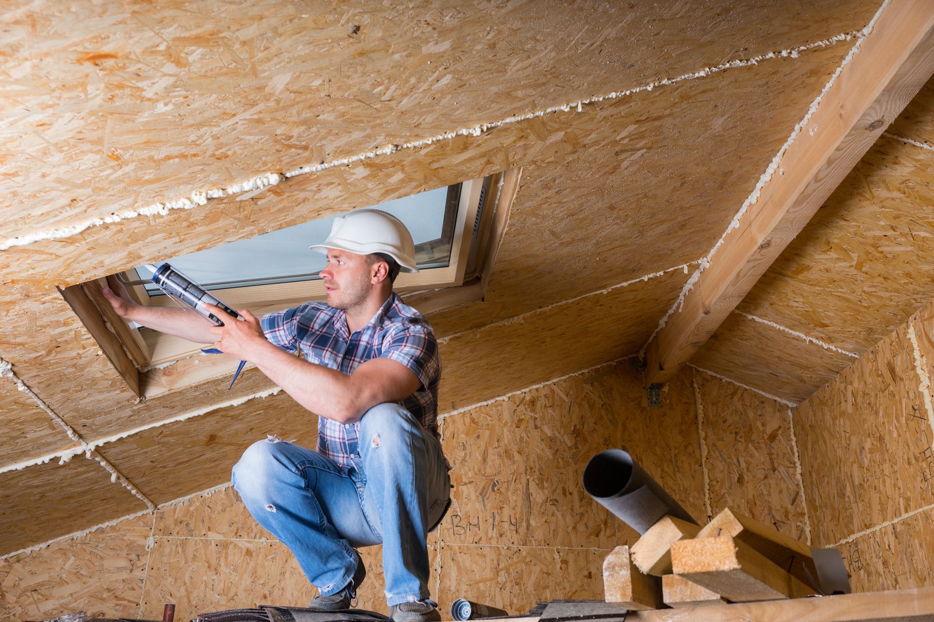 A man is kneeling down in an attic looking through a window.