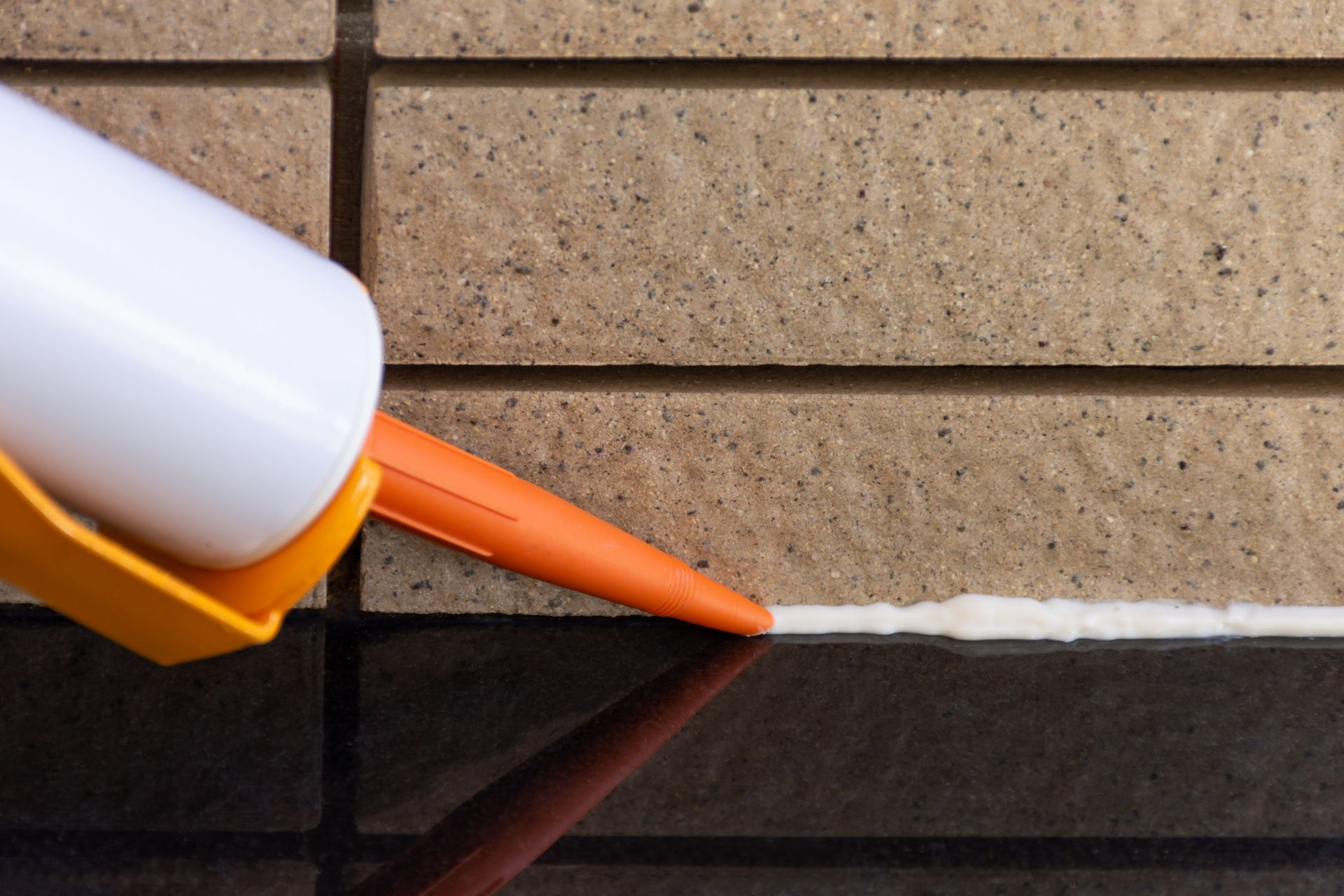 A person is applying silicone sealant to a brick wall.