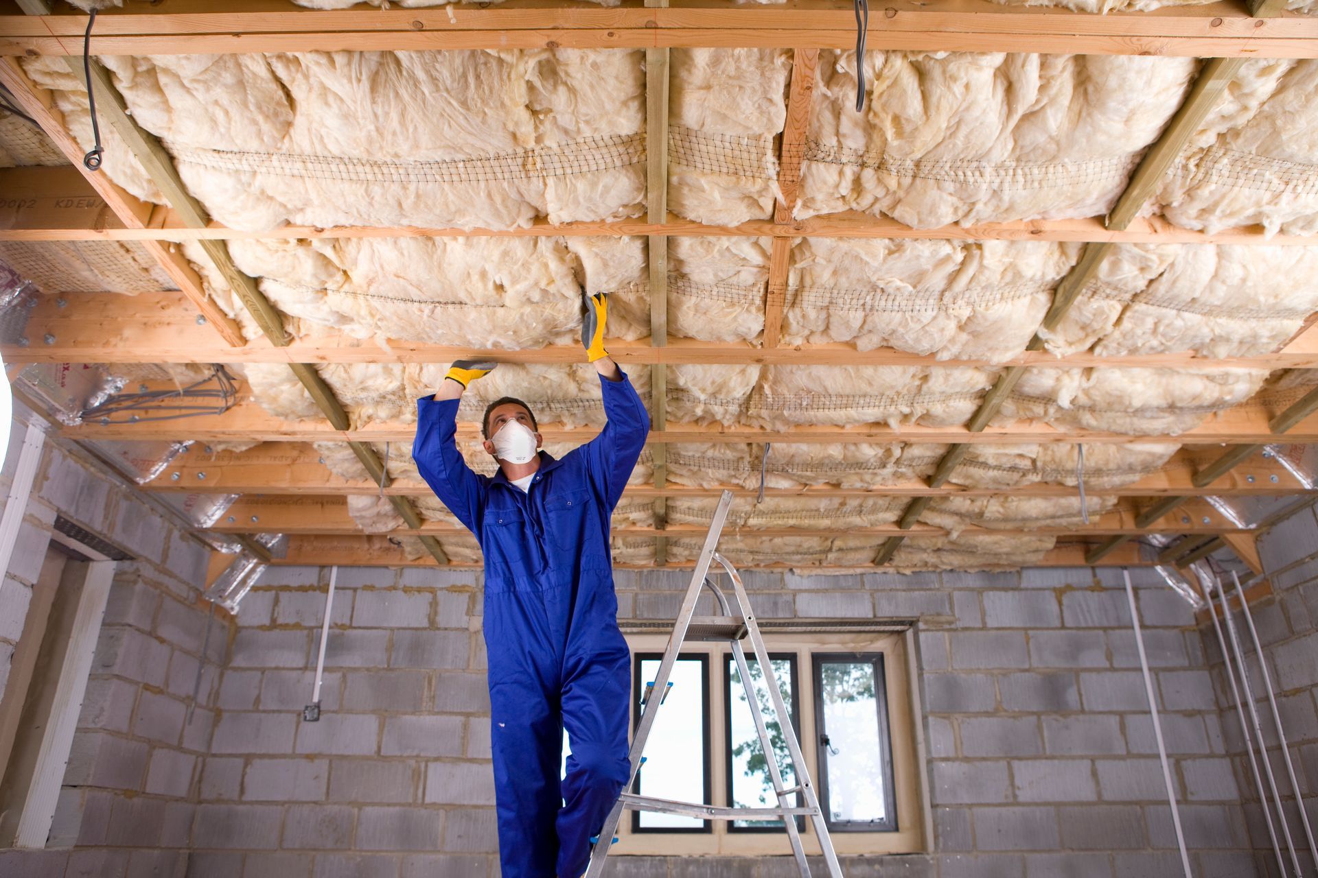 A man wearing a mask is standing on a ladder in a room.