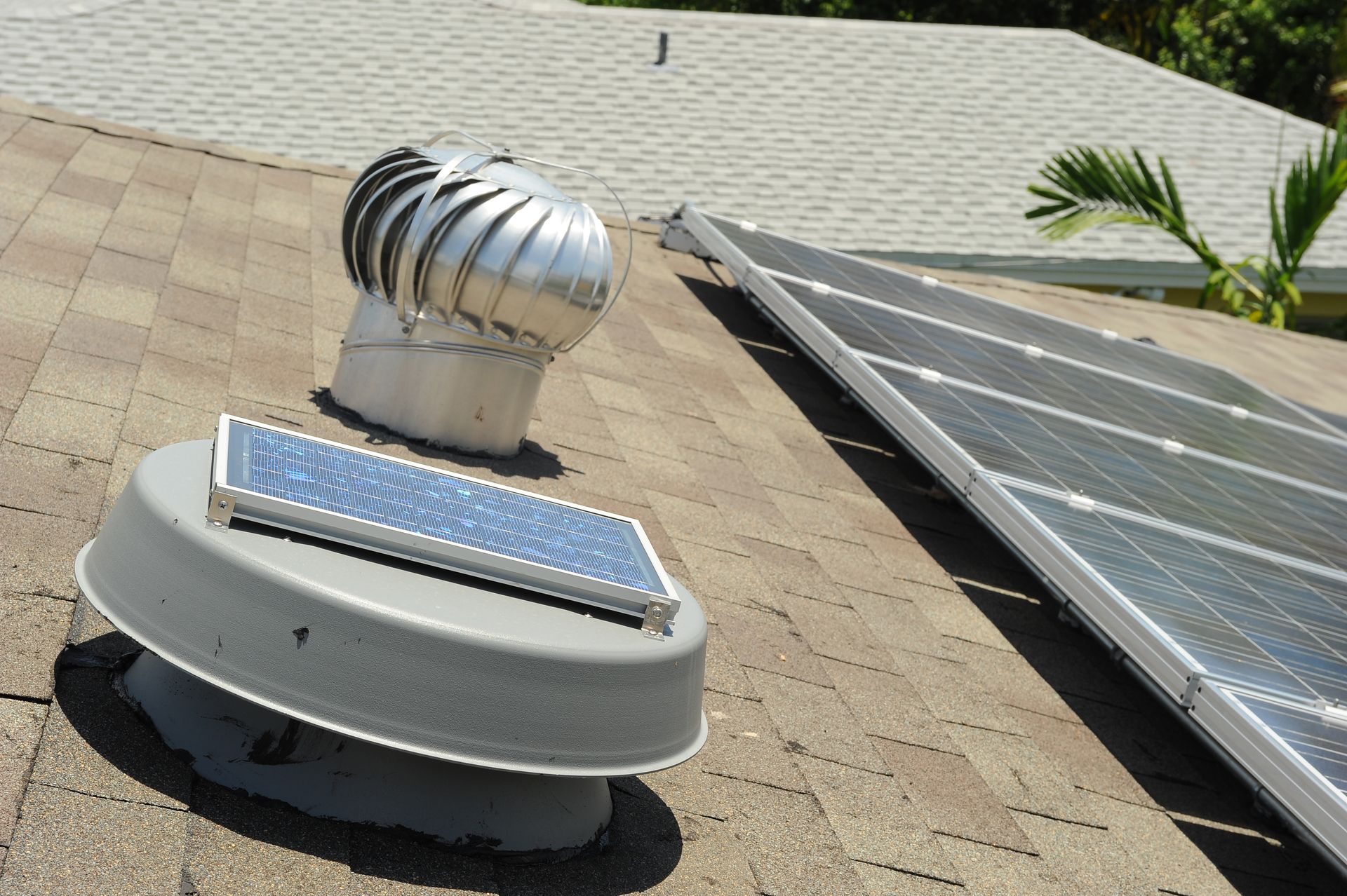 Rooftop solar panels and a silver turbine vent on a shingled roof under bright daylight