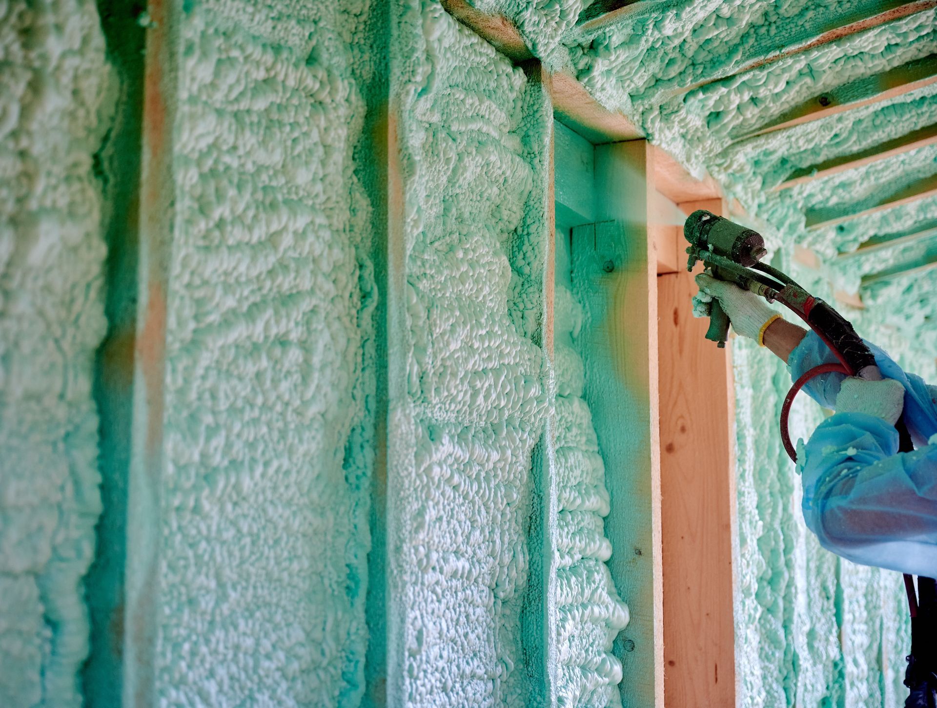Worker spraying foam insulation into wall cavities of a house under construction