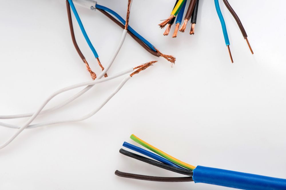 Cables eléctricos expuestos de varios colores, incluidos azul, marrón, negro y amarillo, sobre una superficie blanca.