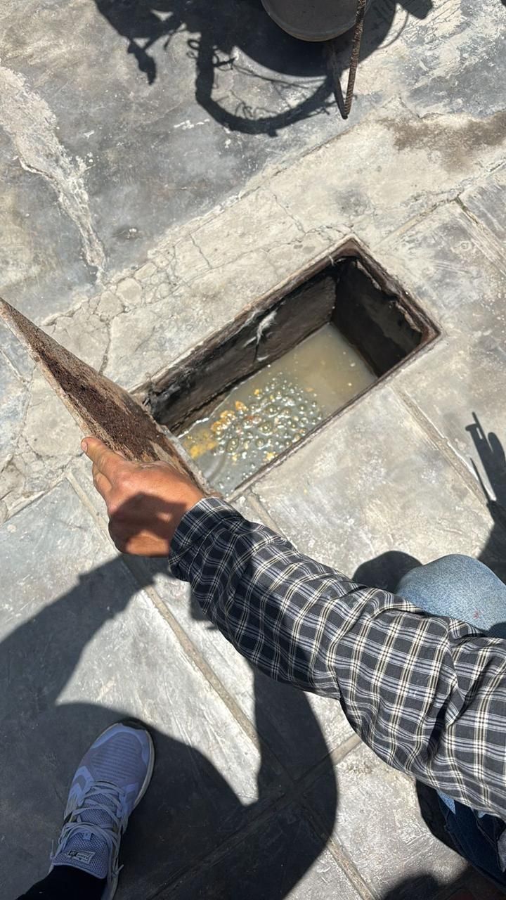 Persona que utiliza una herramienta para examinar una alcantarilla abierta llena de agua turbia.