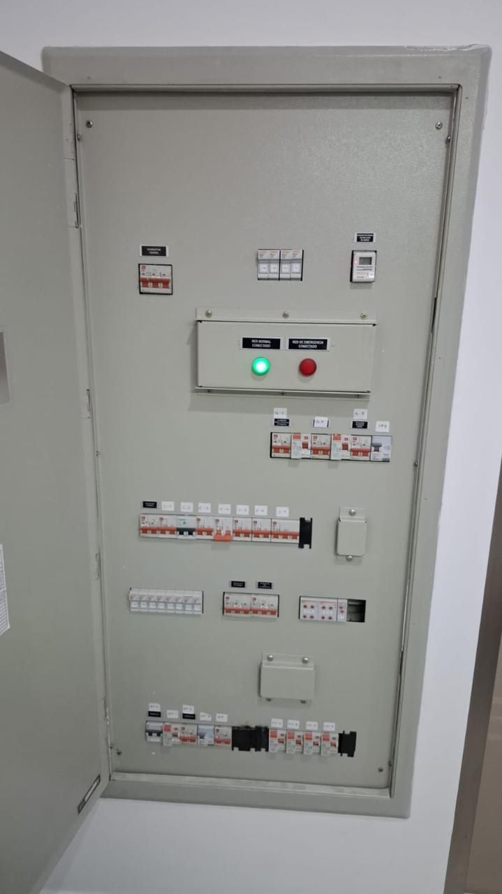 Panel eléctrico con disyuntores, luces indicadoras y botón de encendido, montado en una pared.