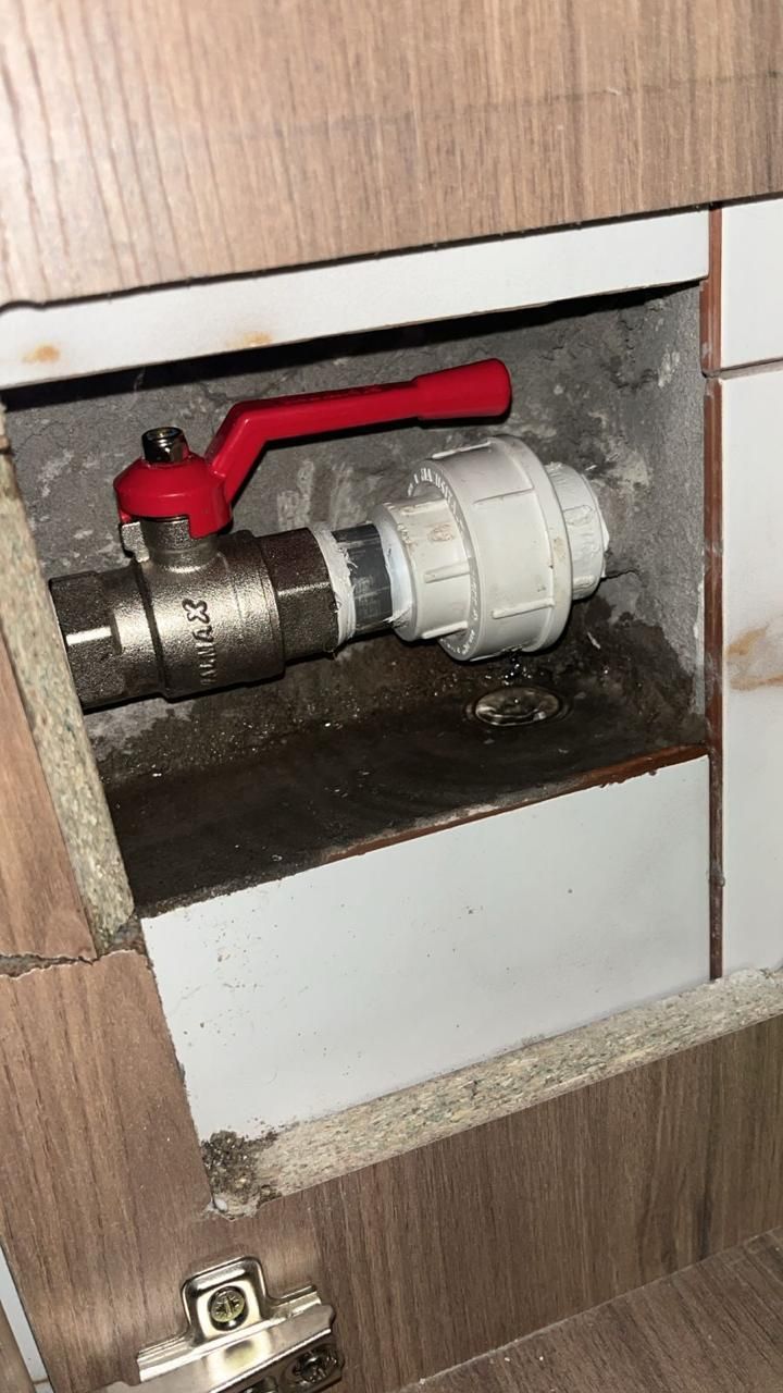 Válvula con manija roja conectada a la plomería dentro de la abertura de un gabinete