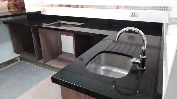 Encimera de granito negro con fregadero y grifo de acero inoxidable en una cocina.