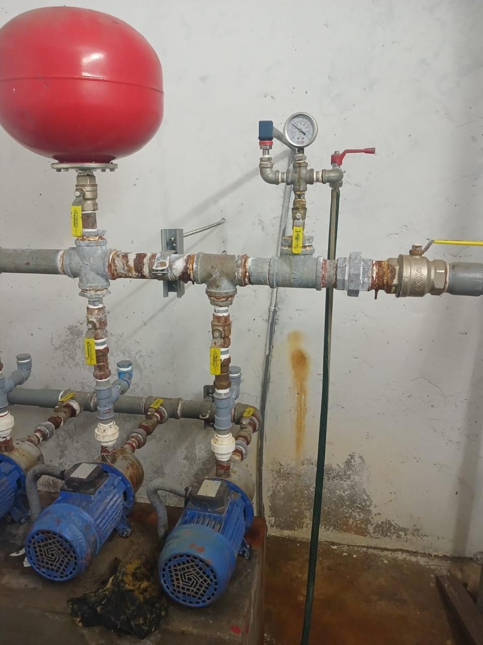 Sistema de bomba de agua con tanque rojo, manómetro y motores azules contra una pared blanca.