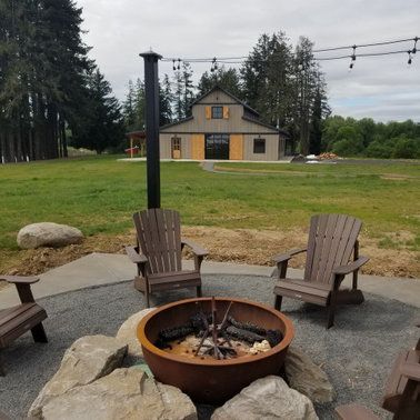 A fire pit with chairs around it in front of a barn.