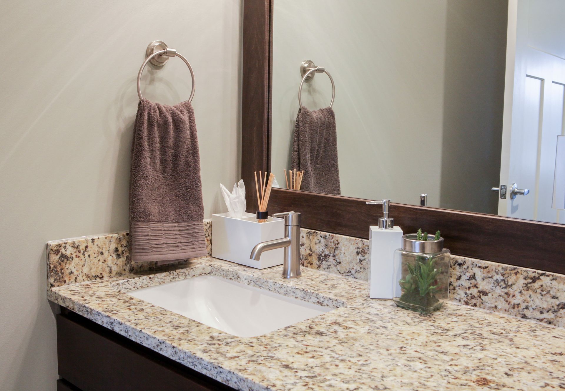 Bathroom vanity with granite countertop, sink, mirror, towel, soap dispenser, and small plant.