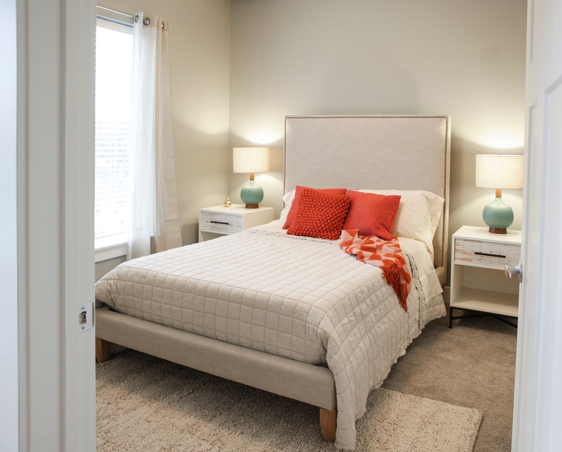 Bright bedroom with a beige bed, white bedding, coral pillows, and matching bedside lamps.