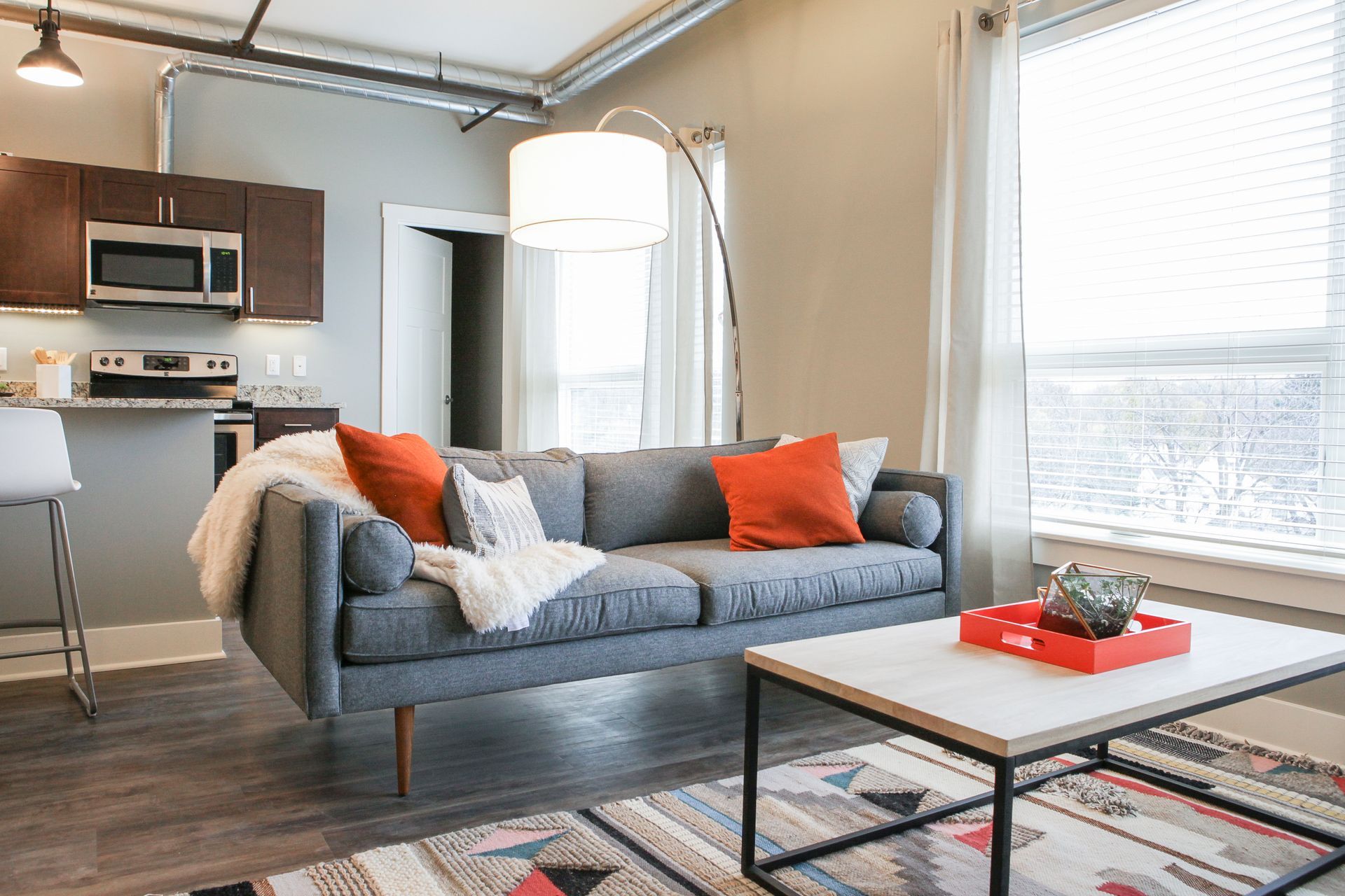 Modern apartment living room with gray sofa, coffee table, pendant light, and kitchen in the background