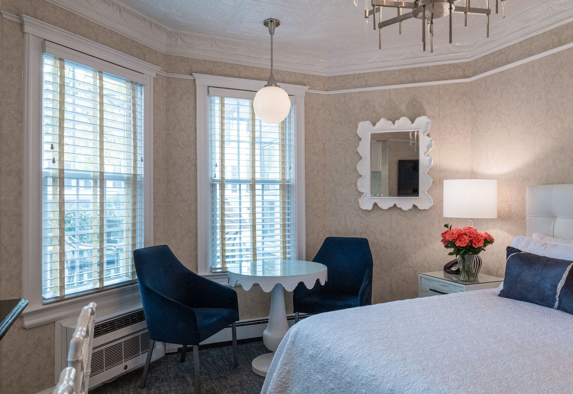 A hotel room with a bed , chairs , a table and a mirror.