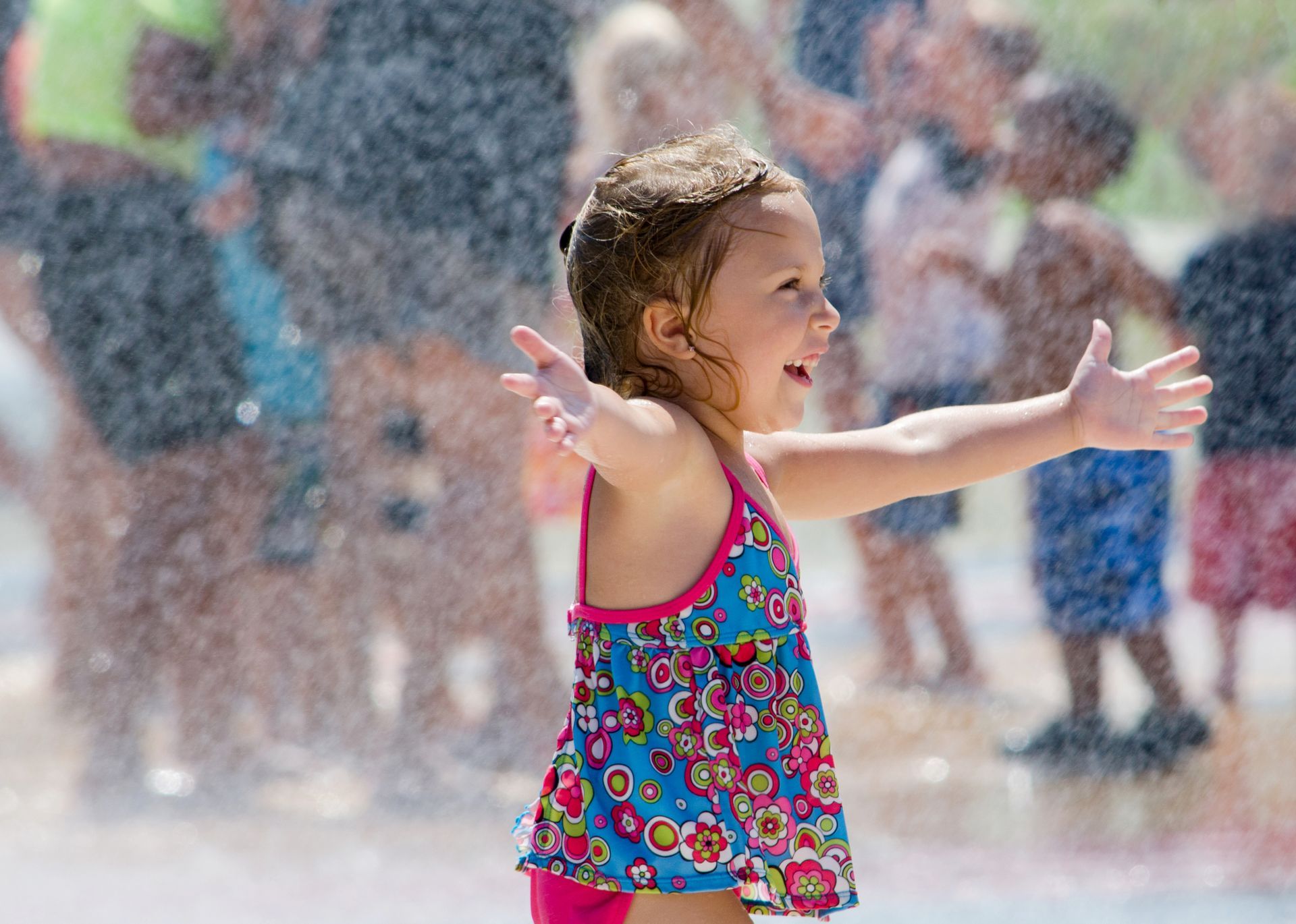 A little girl is playing in a water park with her arms outstretched.