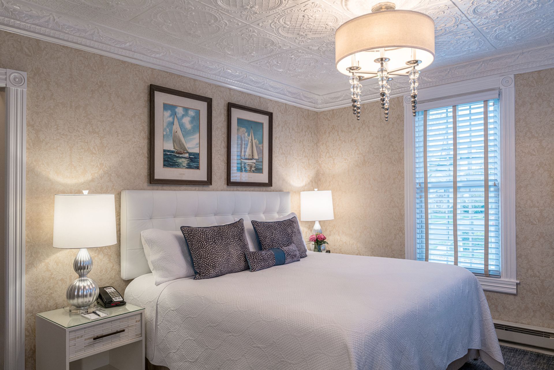 A bedroom with a king size bed , two lamps , two pictures on the wall and a window.