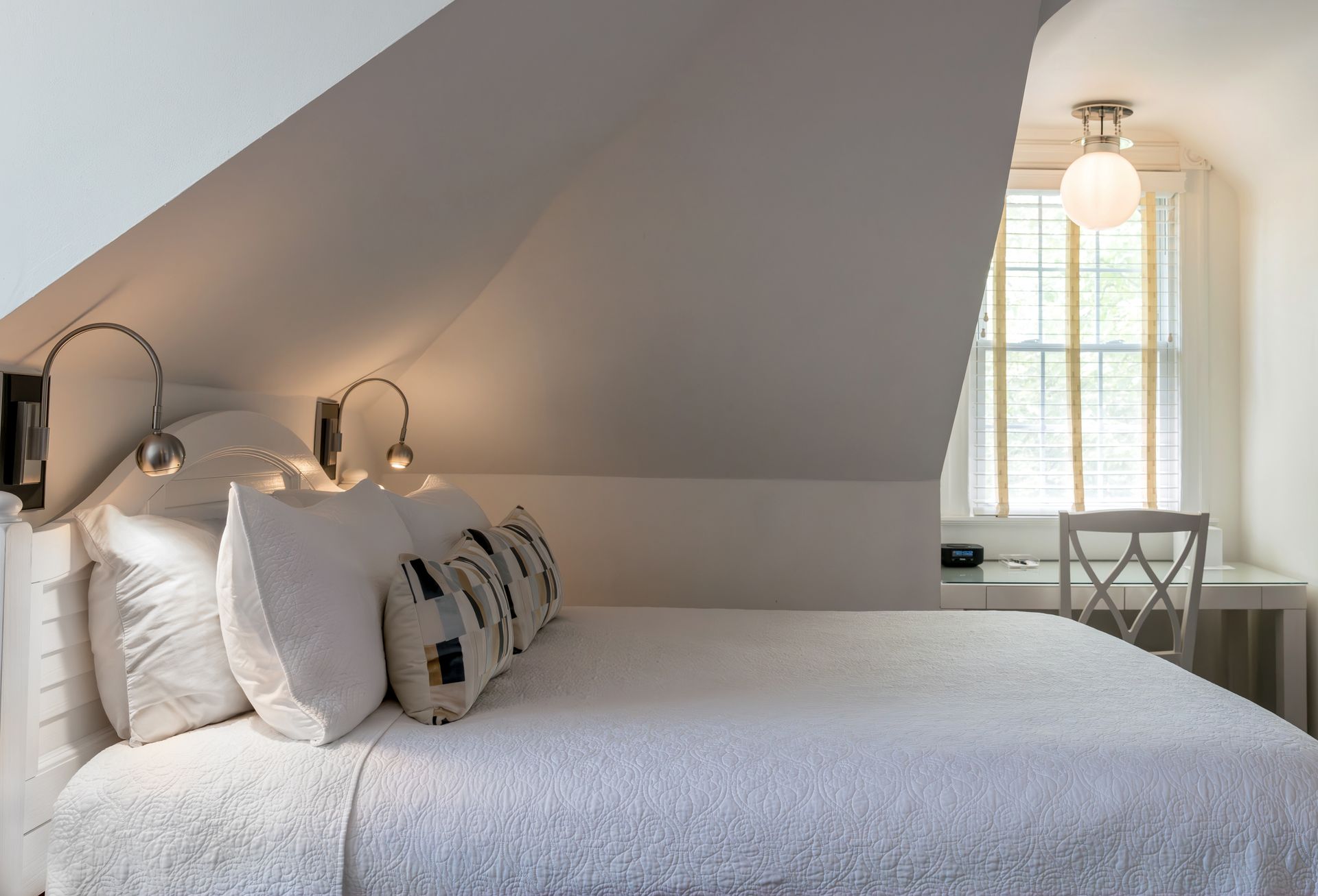 A bedroom with a bed and a desk under a slanted ceiling.