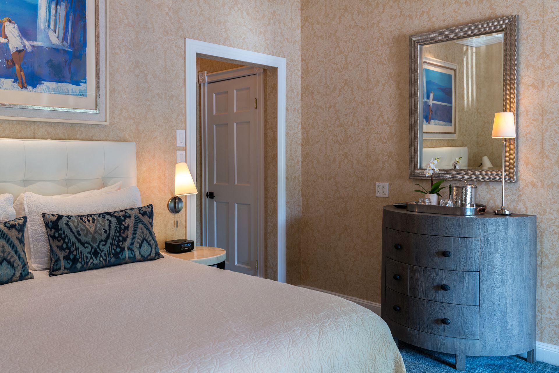A bedroom with a bed , dresser , mirror and painting on the wall.