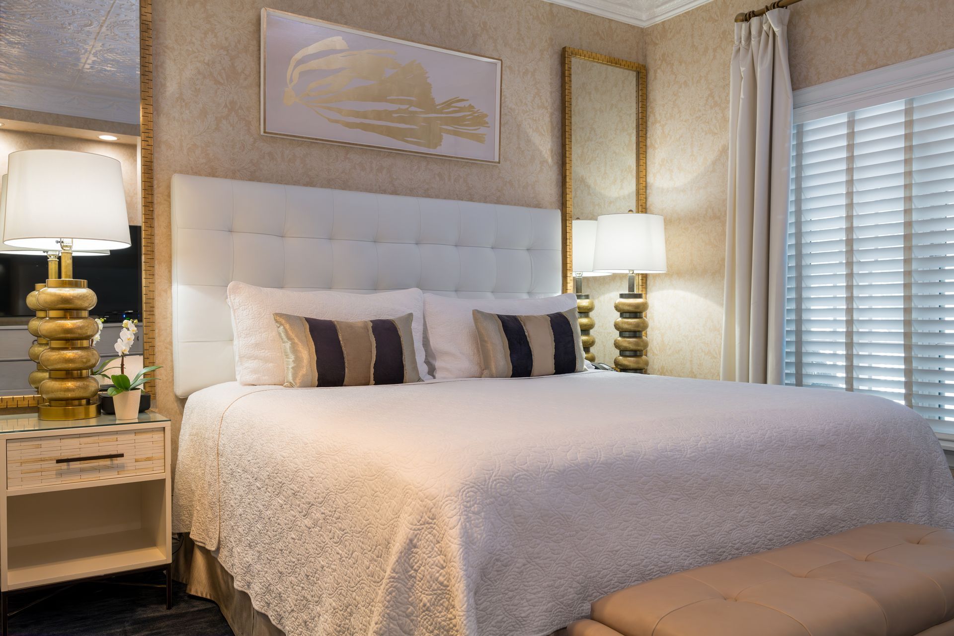 A hotel room with a king size bed , lamps , a bench and a mirror.