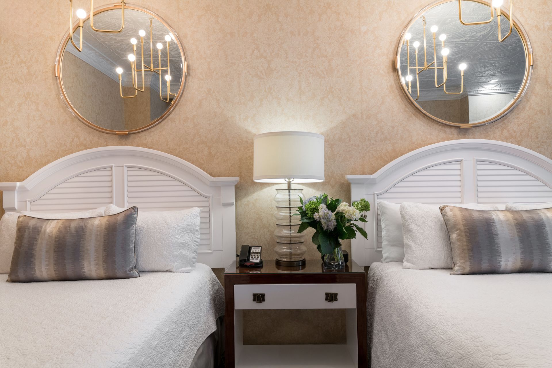 A hotel room with two beds , a nightstand , a lamp and two mirrors.