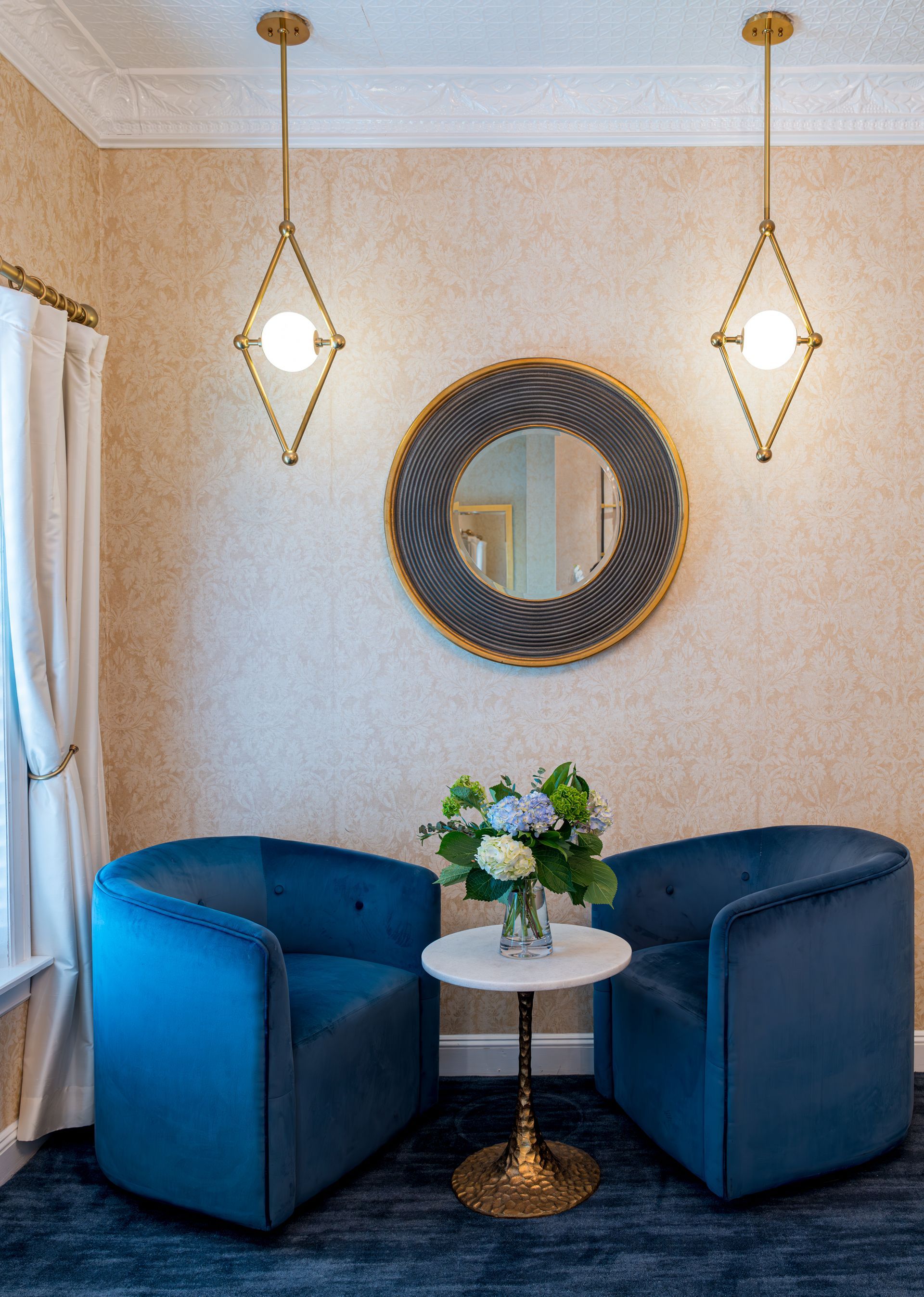 Two blue chairs are sitting next to a table with a vase of flowers on it.
