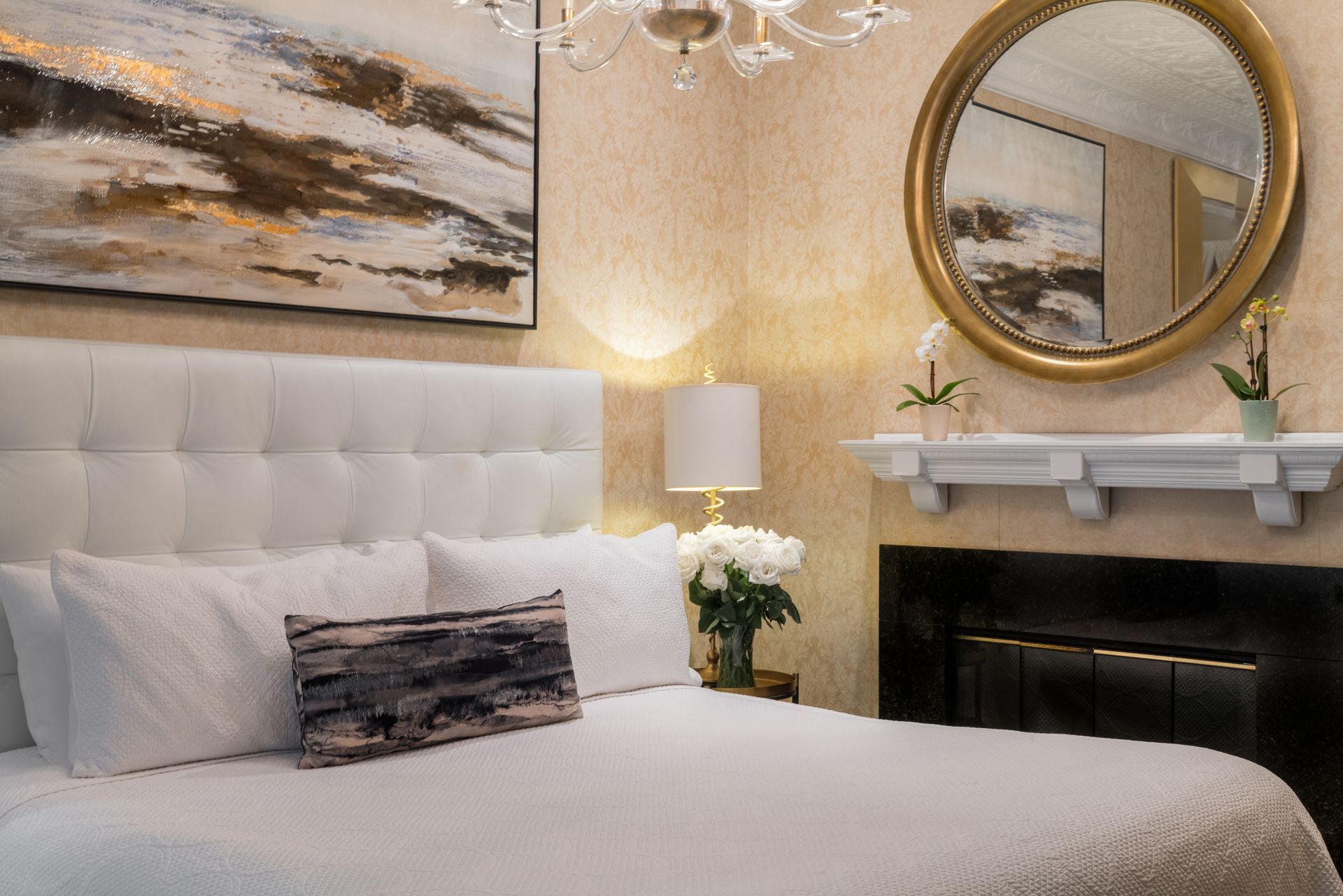 A bedroom with a bed , fireplace , mirror and painting on the wall.